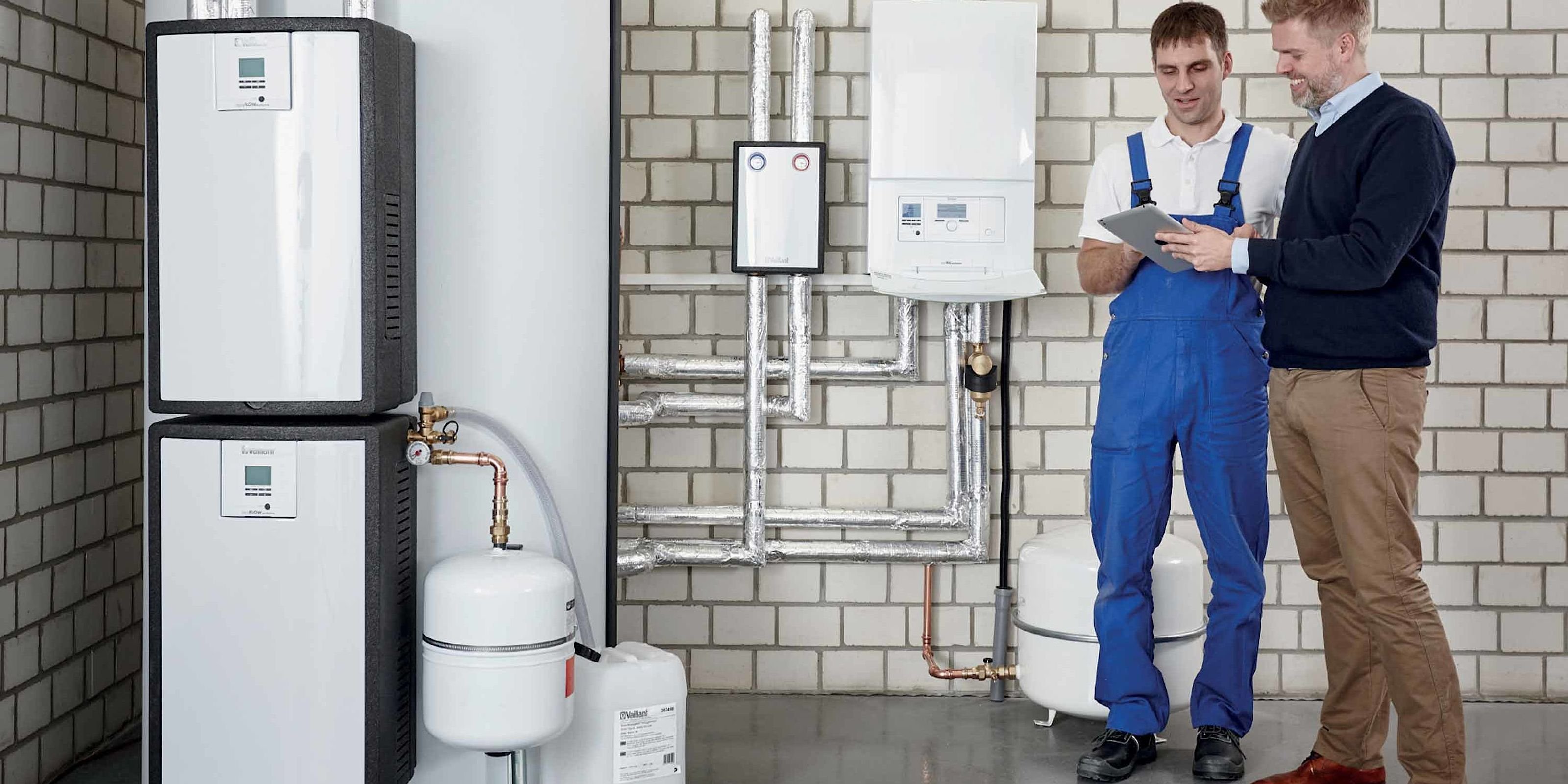 Ein Techniker in blauer Arbeitskleidung und ein Mann in einem Pullover besprechen technische Details auf einem Tablet.