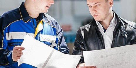 Zwei Männer mit Bauhelm halten eine Zeichnung 