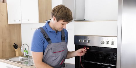 Ein mobiler Elektroniker der eien Backofen überprüft mit einem Messgerät