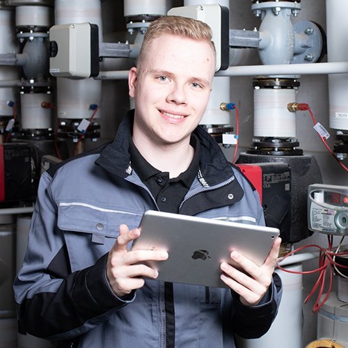 Ein Anlagenmechaniker vor einer Heizungsanlage, der ein Tablet hält