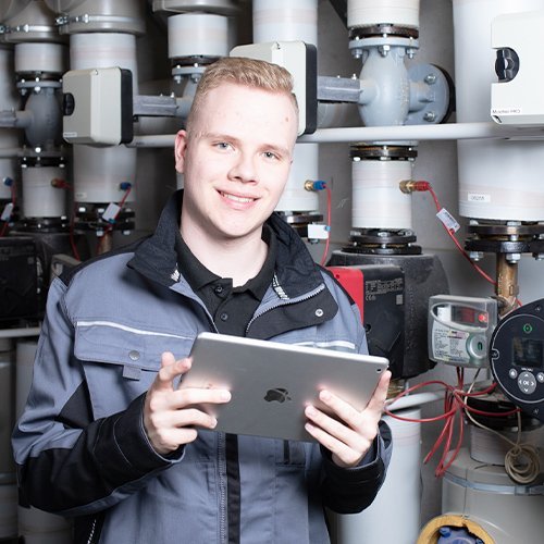 Ein Anlagenmechaniker vor einer Heizungsanlage, der ein Tablet hält 