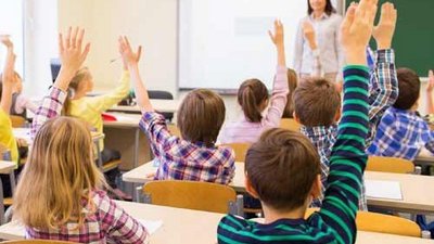 Ein Klassenzimmer in dem viele Schüler ihre Arme hochhalten